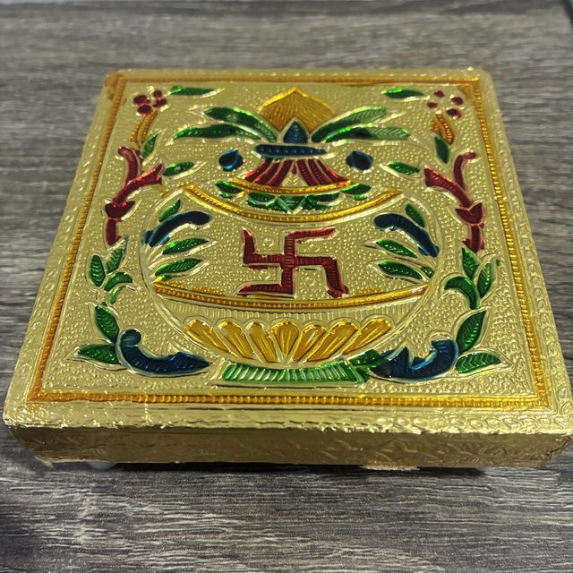A gold meenakari chowki with kalash and swastik design